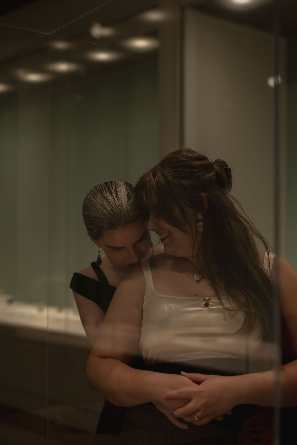 Two people share an intimate embrace in a dimly lit room with soft overhead lighting.