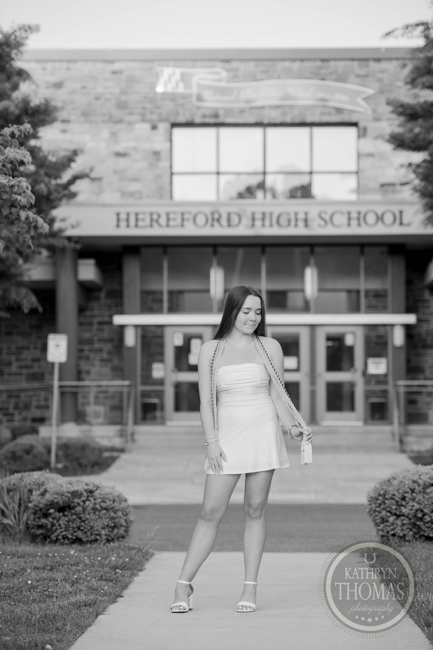 Black and white photo of a student in a white dress posing outside of Hereford High School entrance.