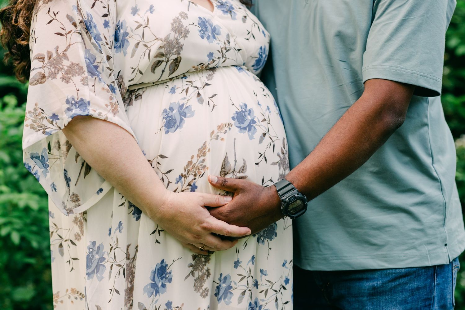 Close-up shot of pregnant belly in floral dress with hands lovingly placed against during a maternity shoot at Southford Falls, CT