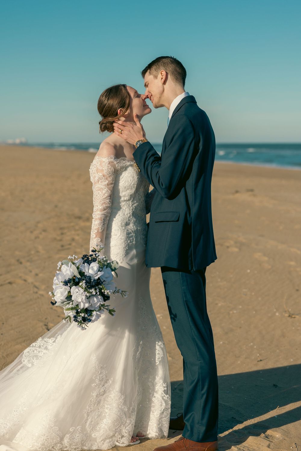 Romantic beach wedding moment as groom tenderly holds bride's face while they share an intimate kiss by the ocean.