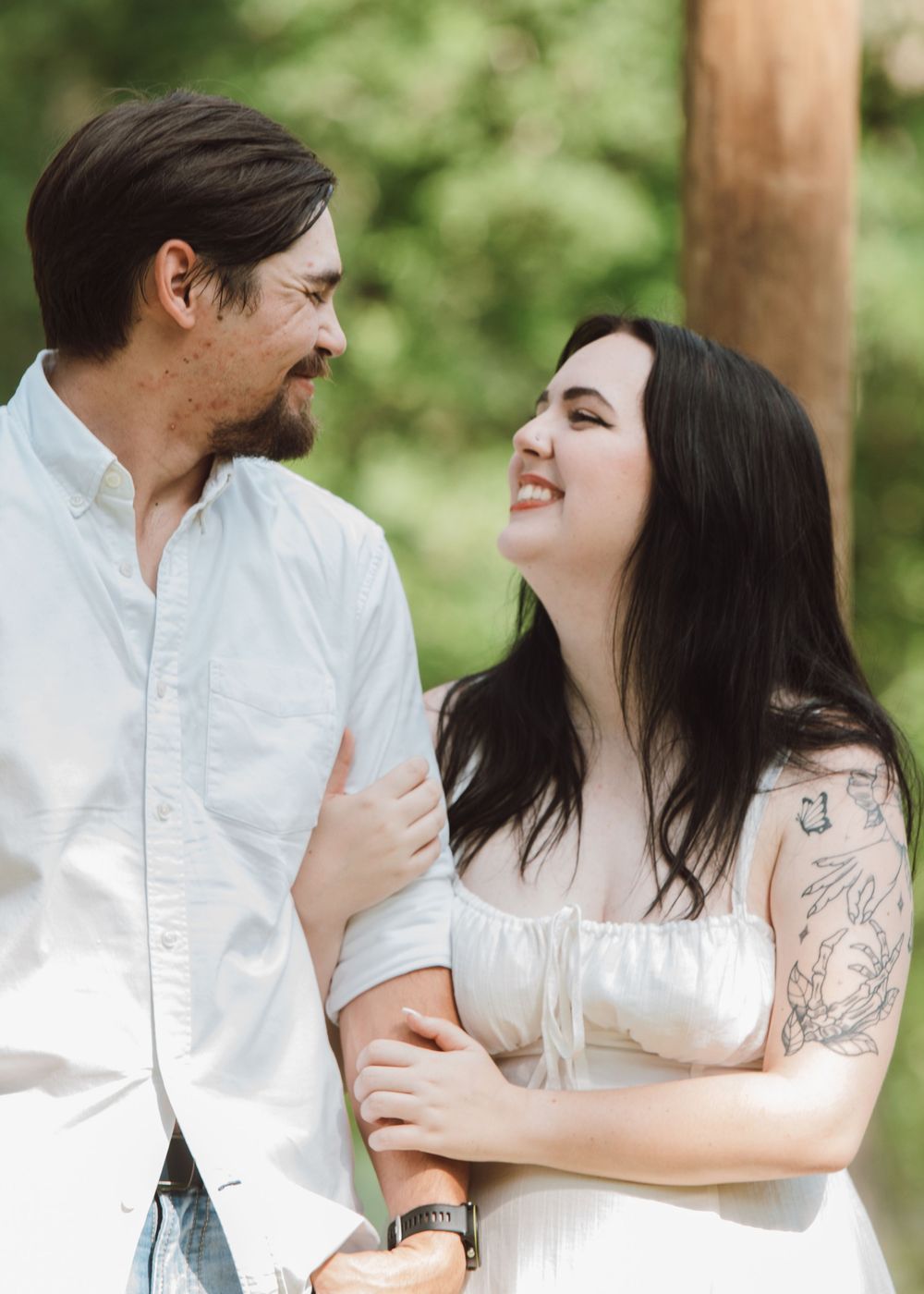 A romantic couple shares a candid laughing moment outdoors with a natural green background.