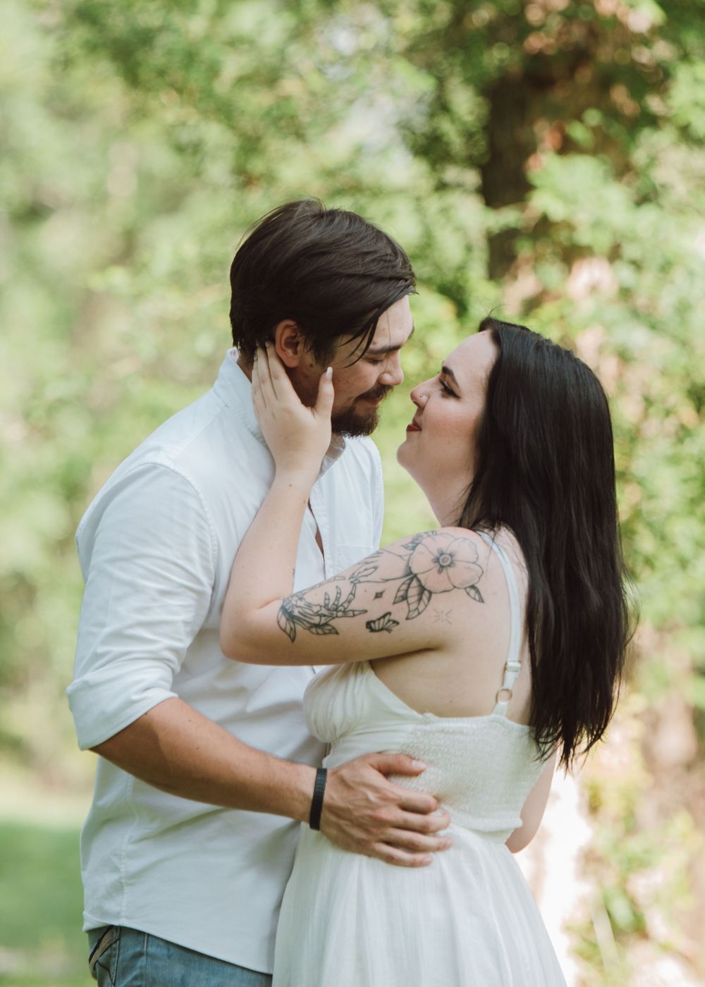 An intimate moment between a couple in white clothing against lush greenery in an outdoor setting.