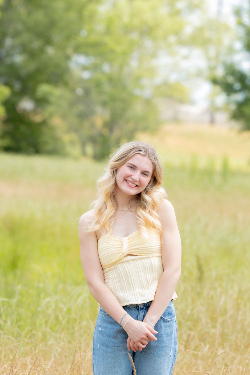 A sunny portrait in tall grass with a yellow top and blue jeans in soft natural lighting.