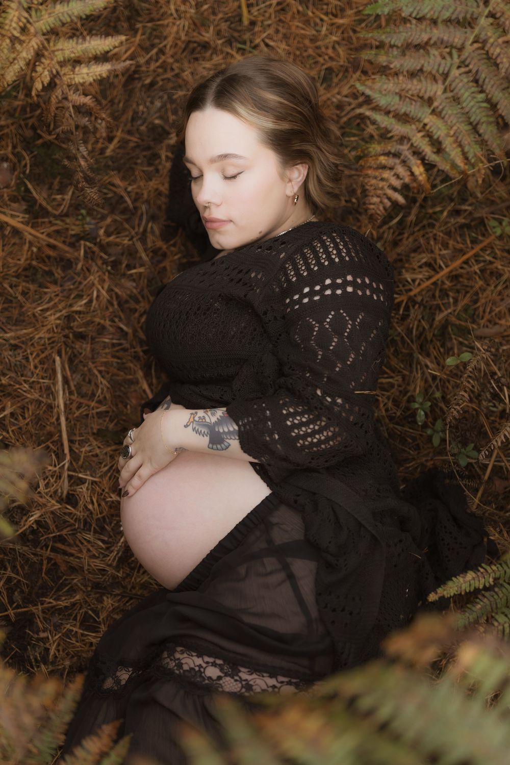 A person in dark clothing rests on autumn forest floor surrounded by ferns and fallen leaves.