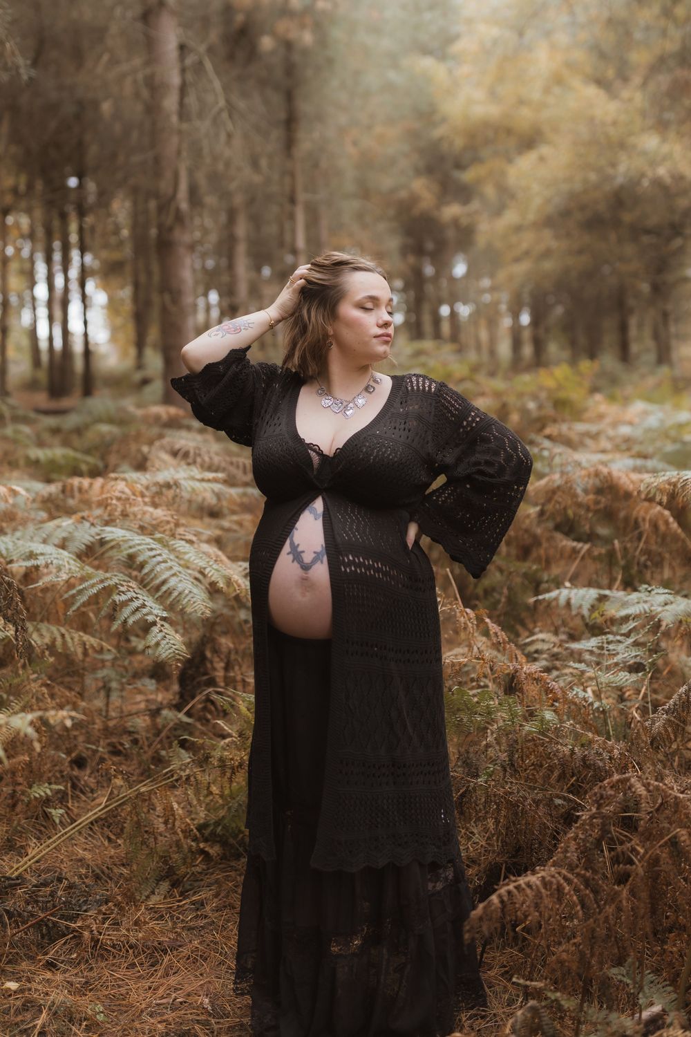 A person in a flowing black dress poses gracefully among autumn ferns in a misty forest setting.