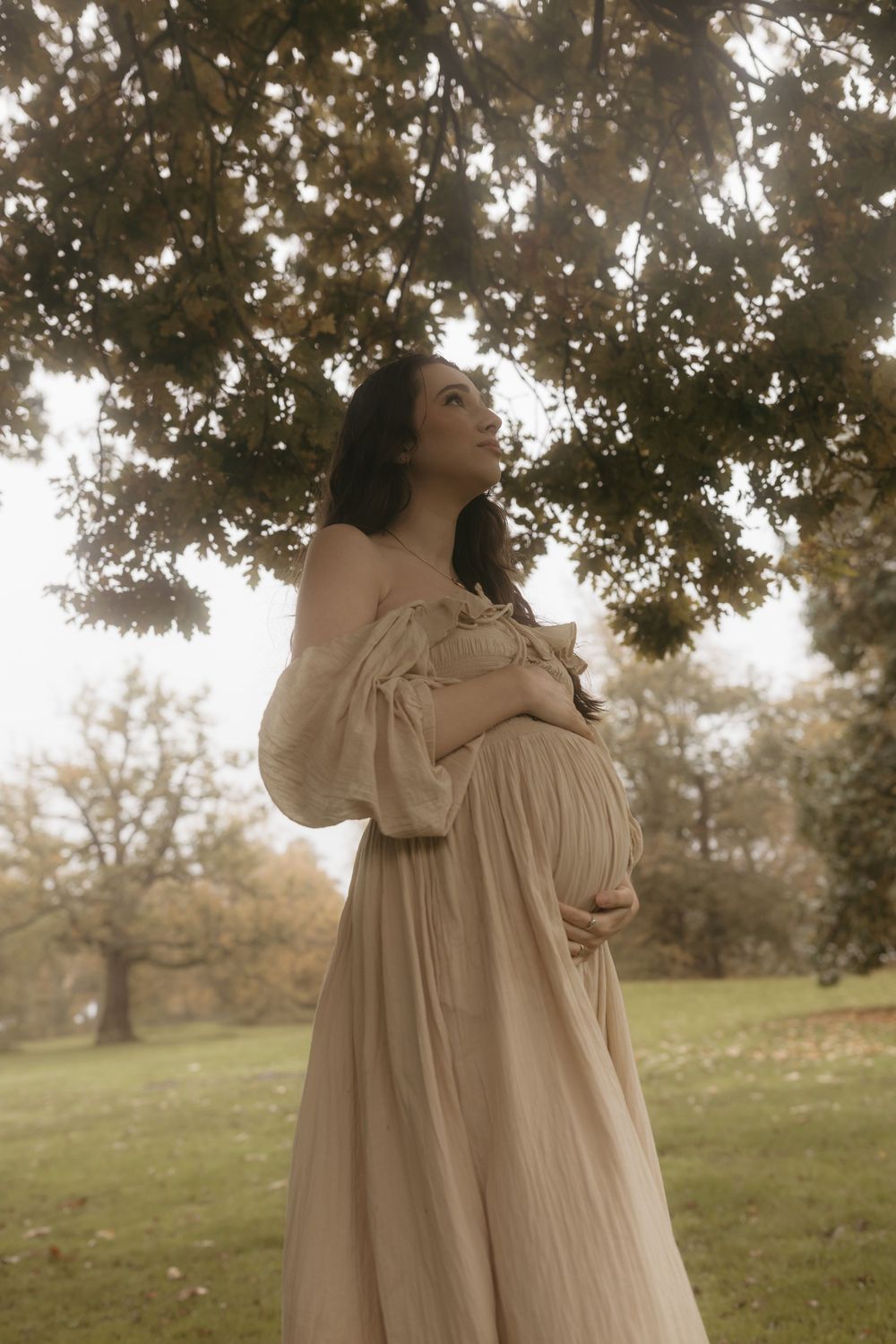 A dreamy portrait series in a field shows someone in a flowing cream dress twirling beneath oak trees at sunset.