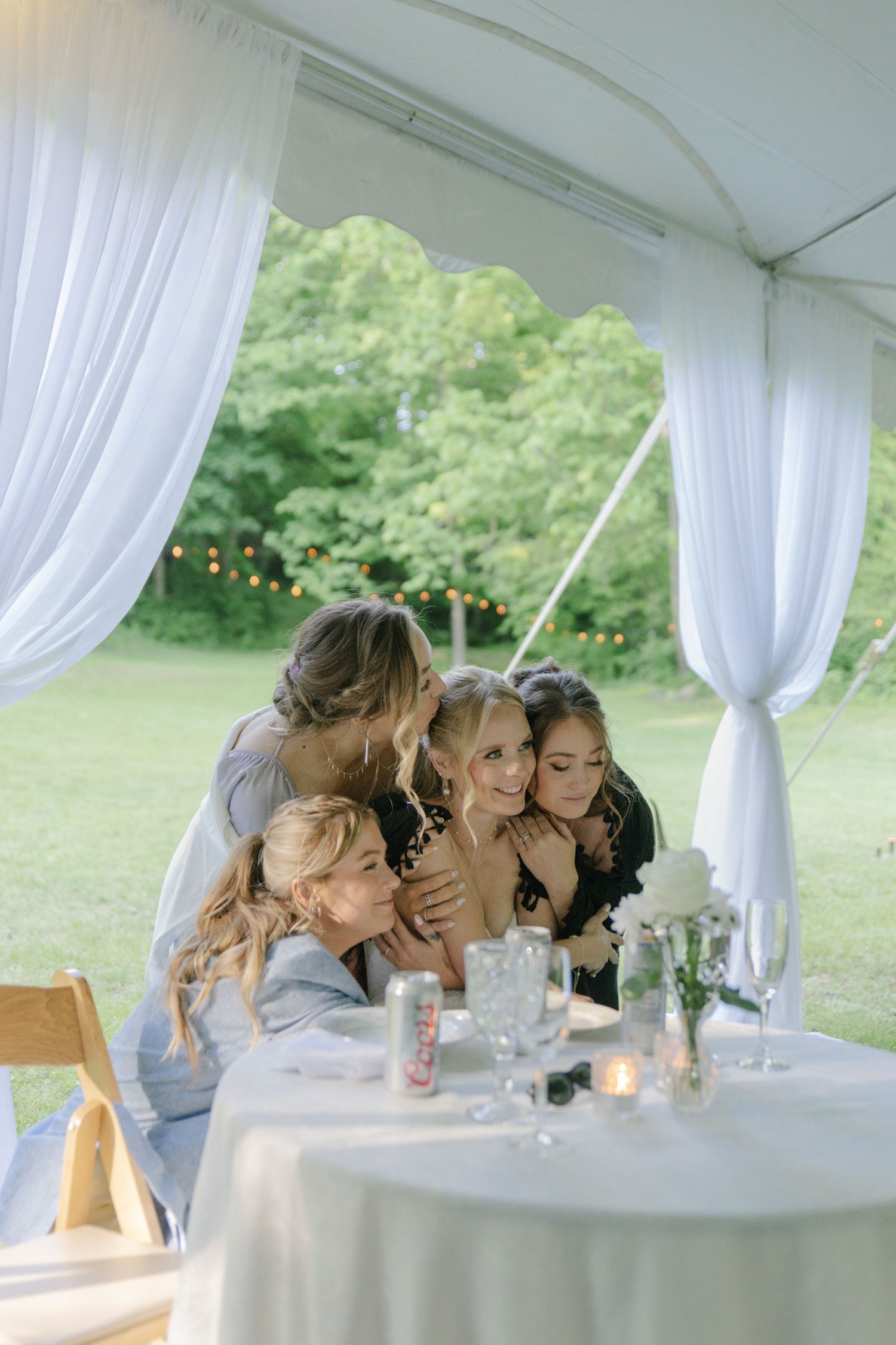 A group shares an intimate moment around a white-clothed table under an outdoor wedding tent.