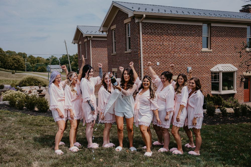 A group poses together on a lawn wearing matching light pink robes outside a brick building in celebration.