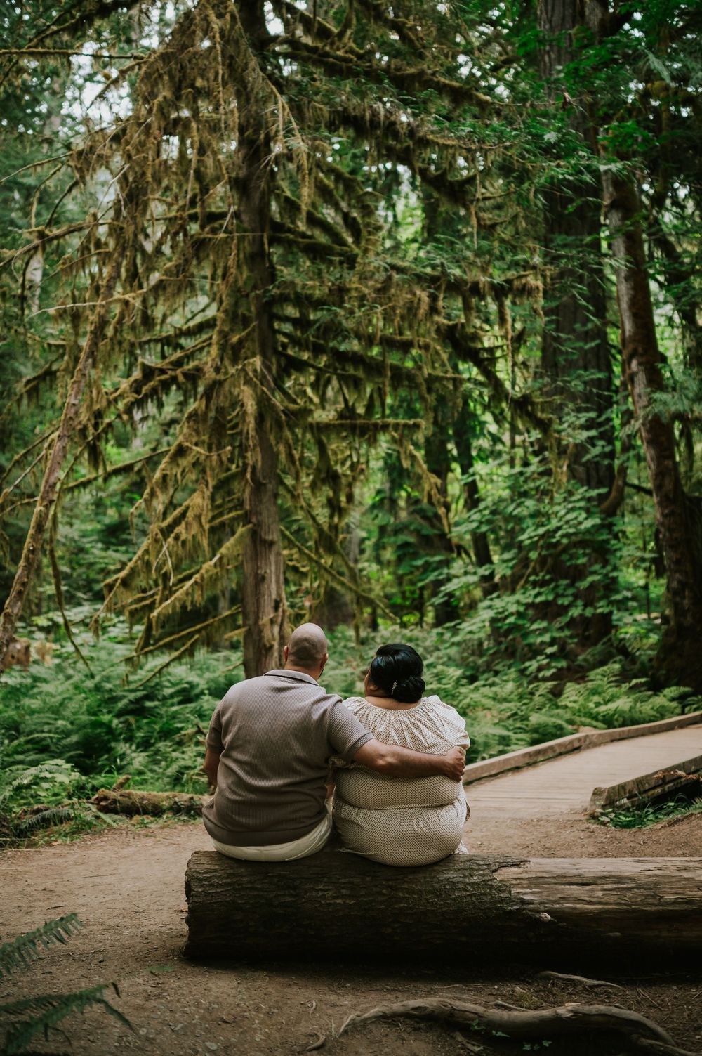 Photo of engaged couple sitting on log in Cathedral Groves, MacMillan Park forest trails. Vancouver Island adventure photographer
