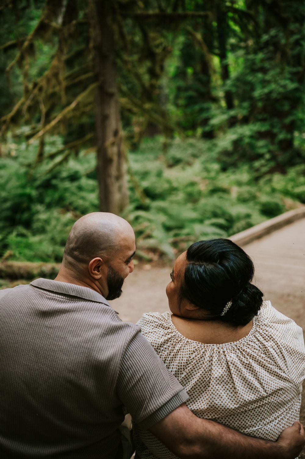 Photo of engaged couple sitting on log smiling in Cathedral Groves, MacMillan Park forest trails. Vancouver Island adventure photographer