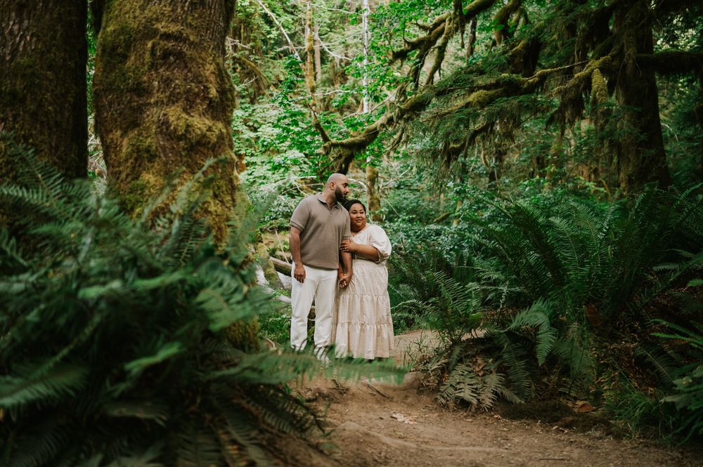 Photo of engaged couple holding each other in Cathedral Groves, MacMillan Park forest trails by fern Vancouver Island adventure photographer