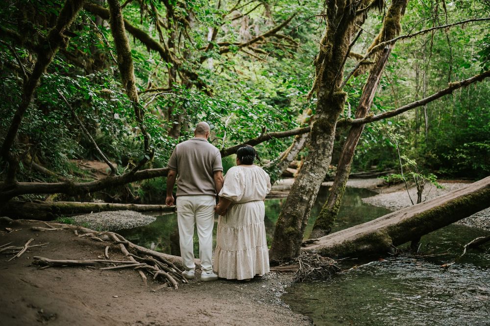 Photo of engaged couple standing in front of creek in forest of Cathedral Groves, MacMillan Park. Vancouver Island adventure photographer
