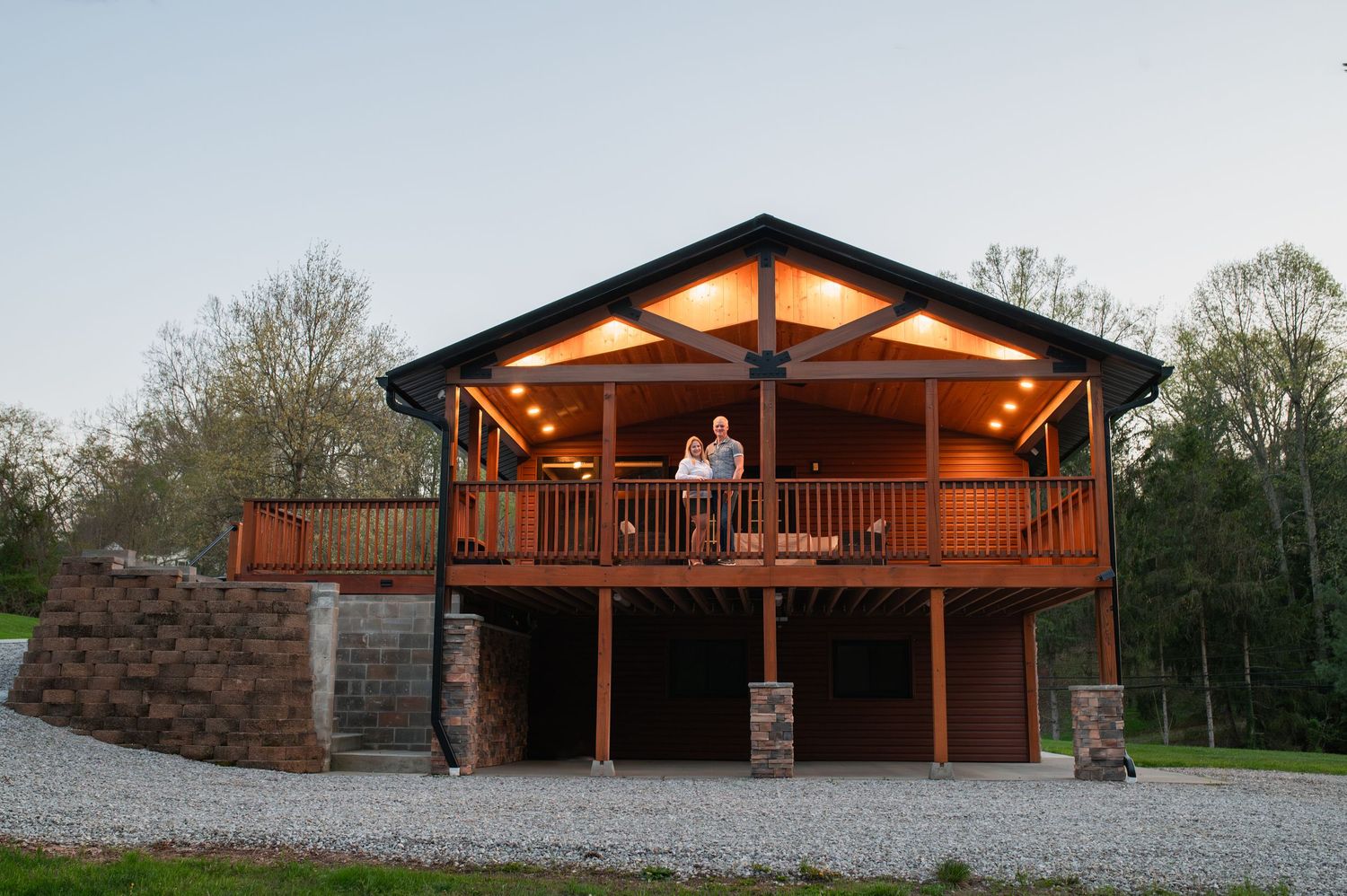 A rustic wooden cabin with a lit porch and balcony at dusk.