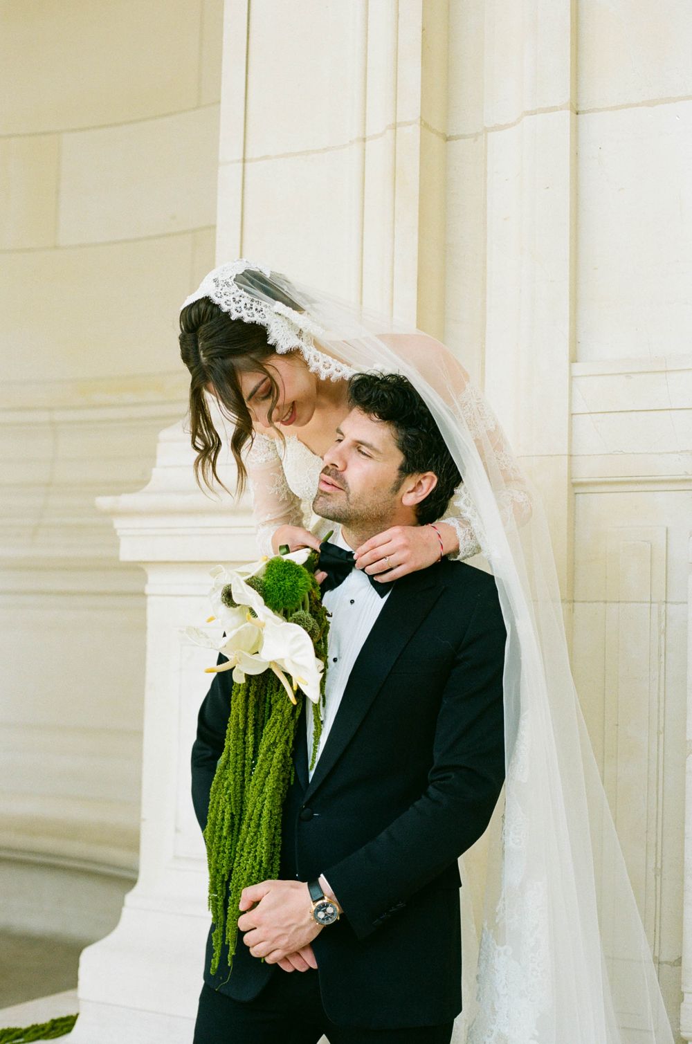 A romantic wedding moment with a bride in a flowing veil embracing the groom in a black suit. Paris editorial wedding photos. Paris film