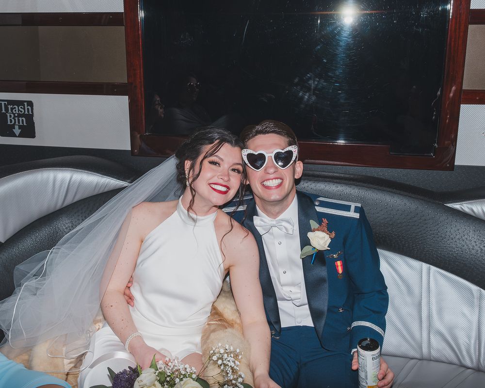 A newlywed couple shares a joyful moment in formalwear inside a vehicle.