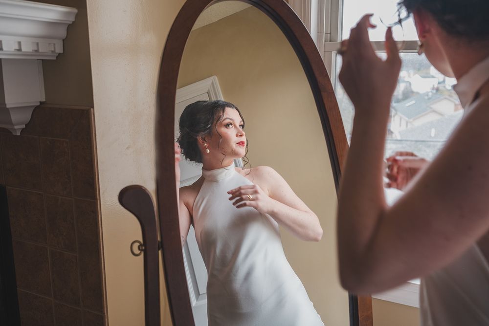 Reflection of person getting ready in round vintage mirror with elegant white dress.