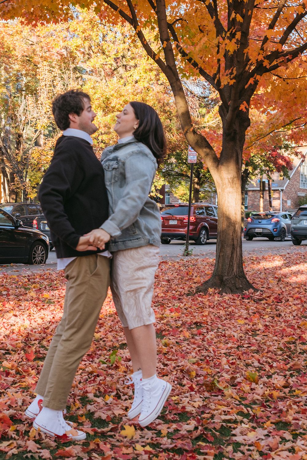 A couple in casual attire standing close together among vibrant fall foliage.