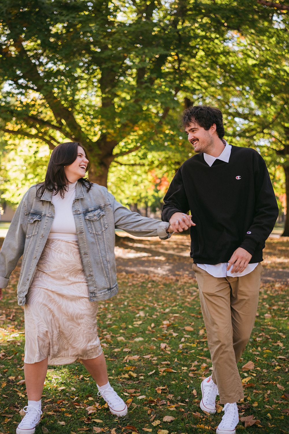A couple playfully walking and laughing together on fallen autumn leaves in a park.