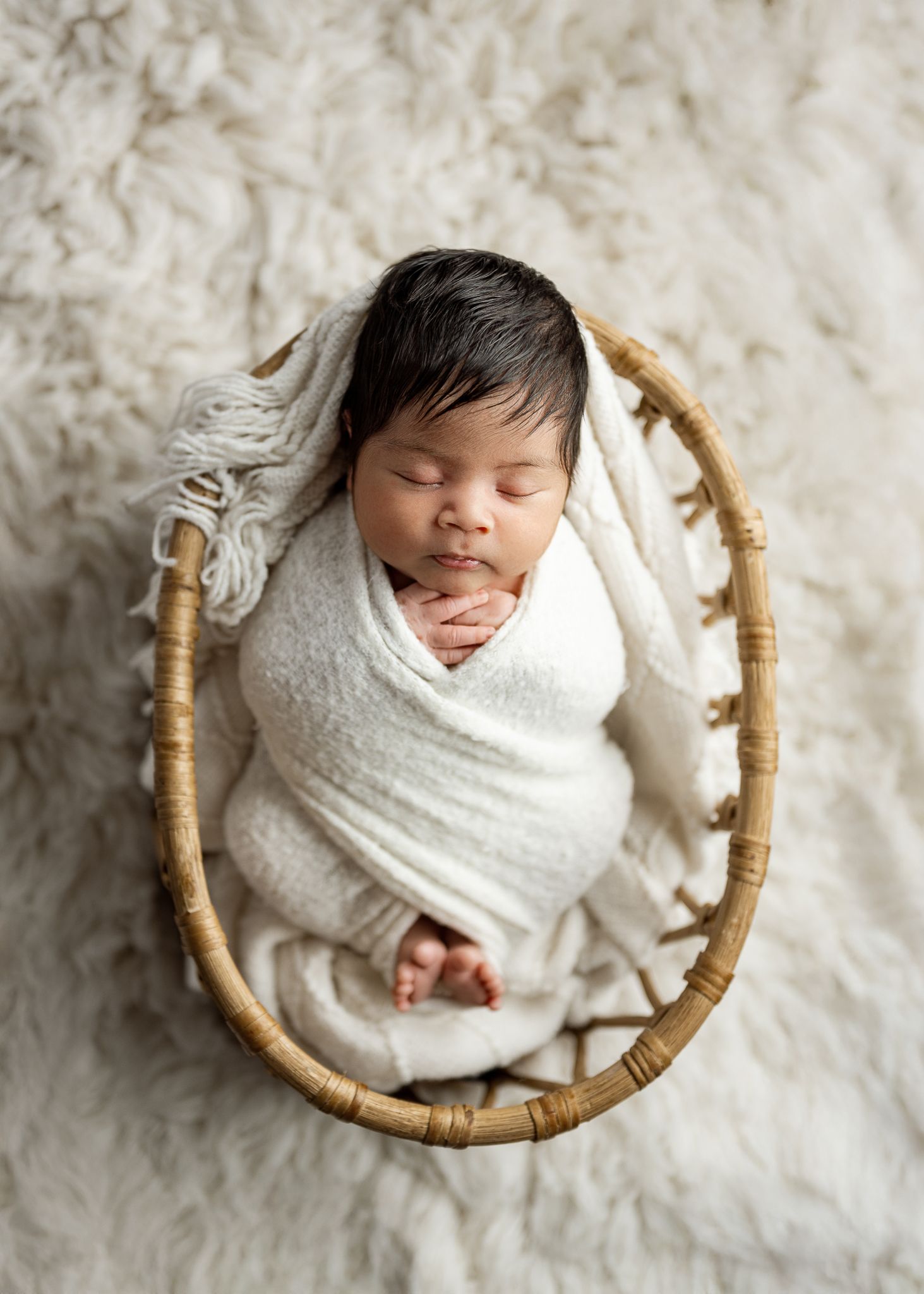 Peacefully sleeping newborn wrapped in white swaddle blanket nestled in small woven basket on textured background.