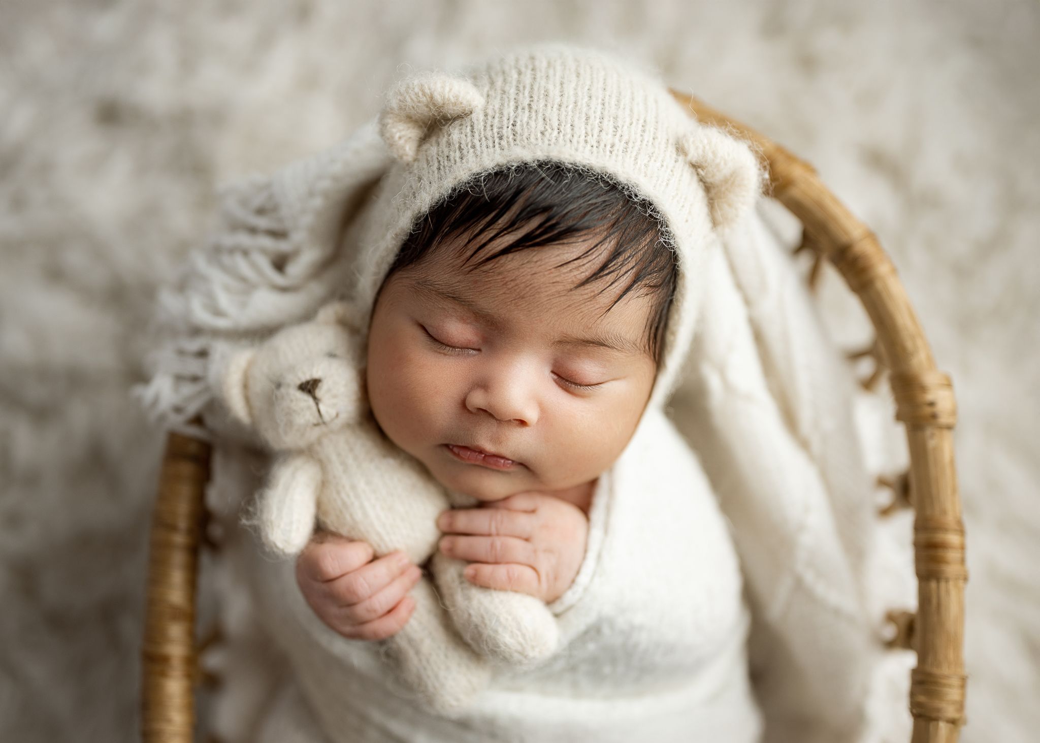Sleeping newborn wrapped in white blanket rests gently in woven wicker basket during photo session.