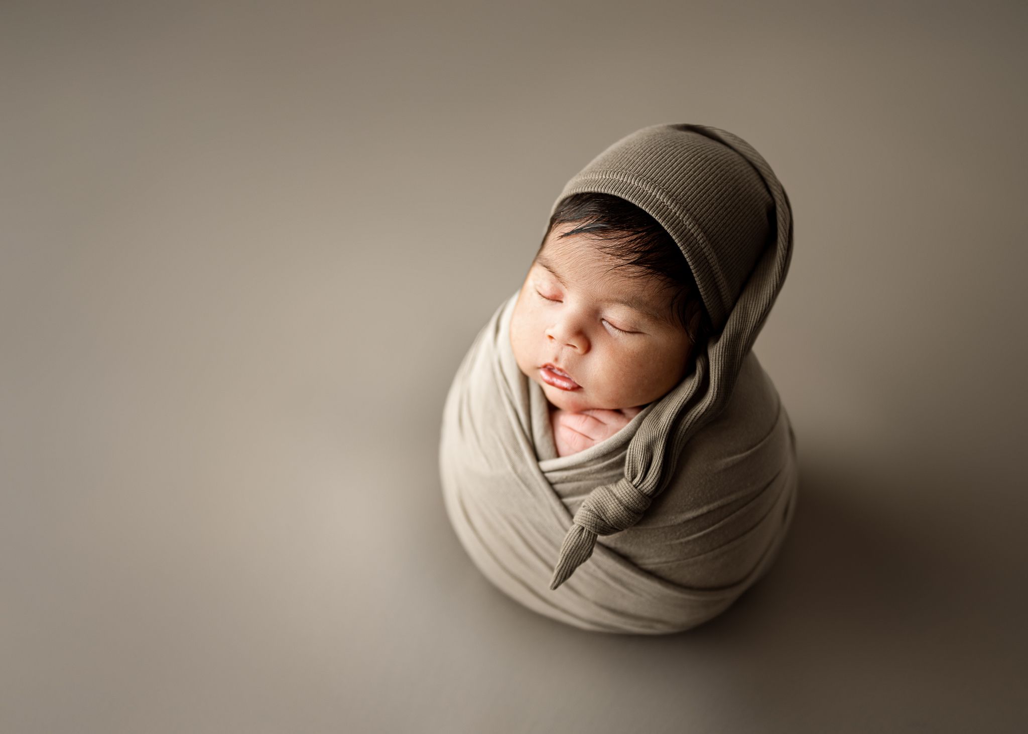 A sleeping newborn swaddled in grey fabric photographed on a neutral grey backdrop.