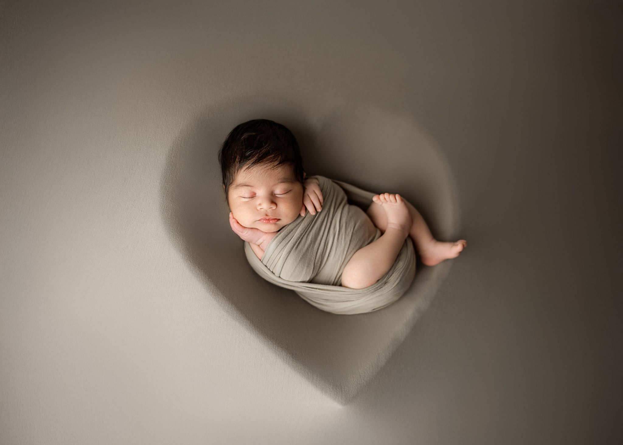 Small baby sleeps peacefully under soft lighting in minimalist newborn photo session.