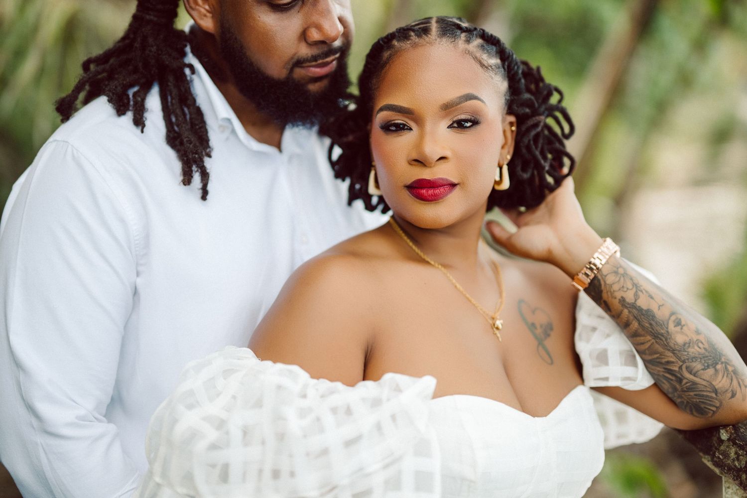 A couple in wedding attire share an intimate moment outdoors, with the bride in a strapless white dress and detailed hairstyle.