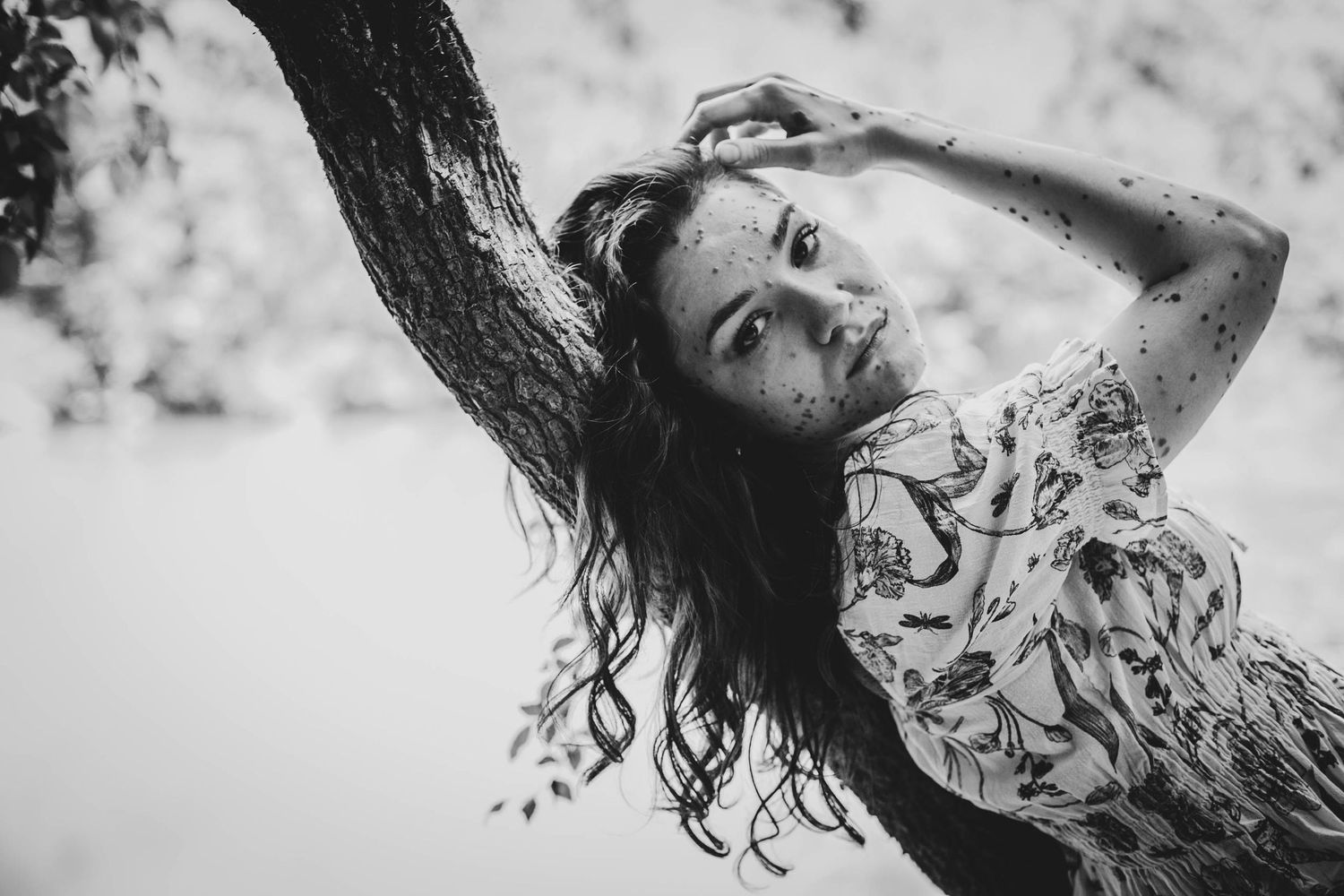 Black and white artistic portrait showing long wavy hair and floral printed dress against a light ethereal background.
