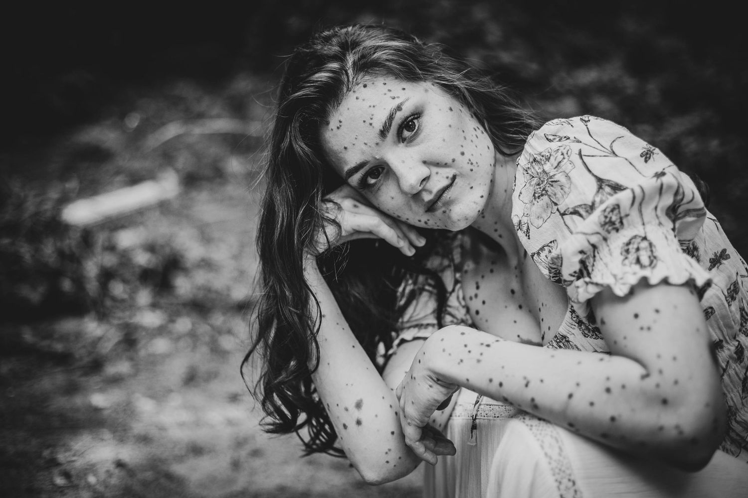 A black and white artistic photograph shows someone lying on dried leaves, creating a moody and ethereal composition.