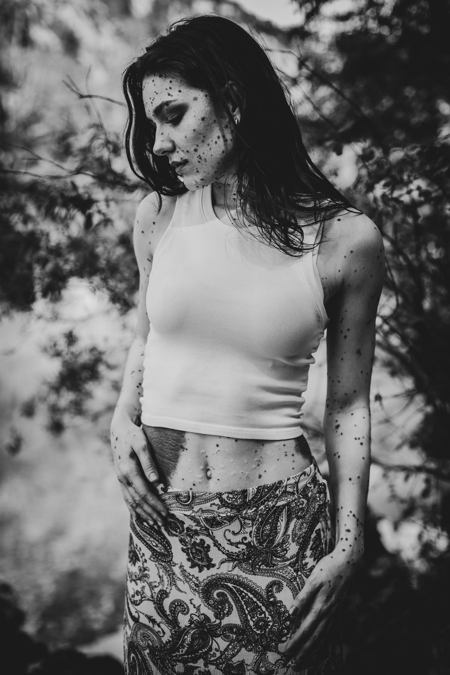 Black and white artistic portrait of someone in a crop top and patterned skirt with water droplets on their skin.