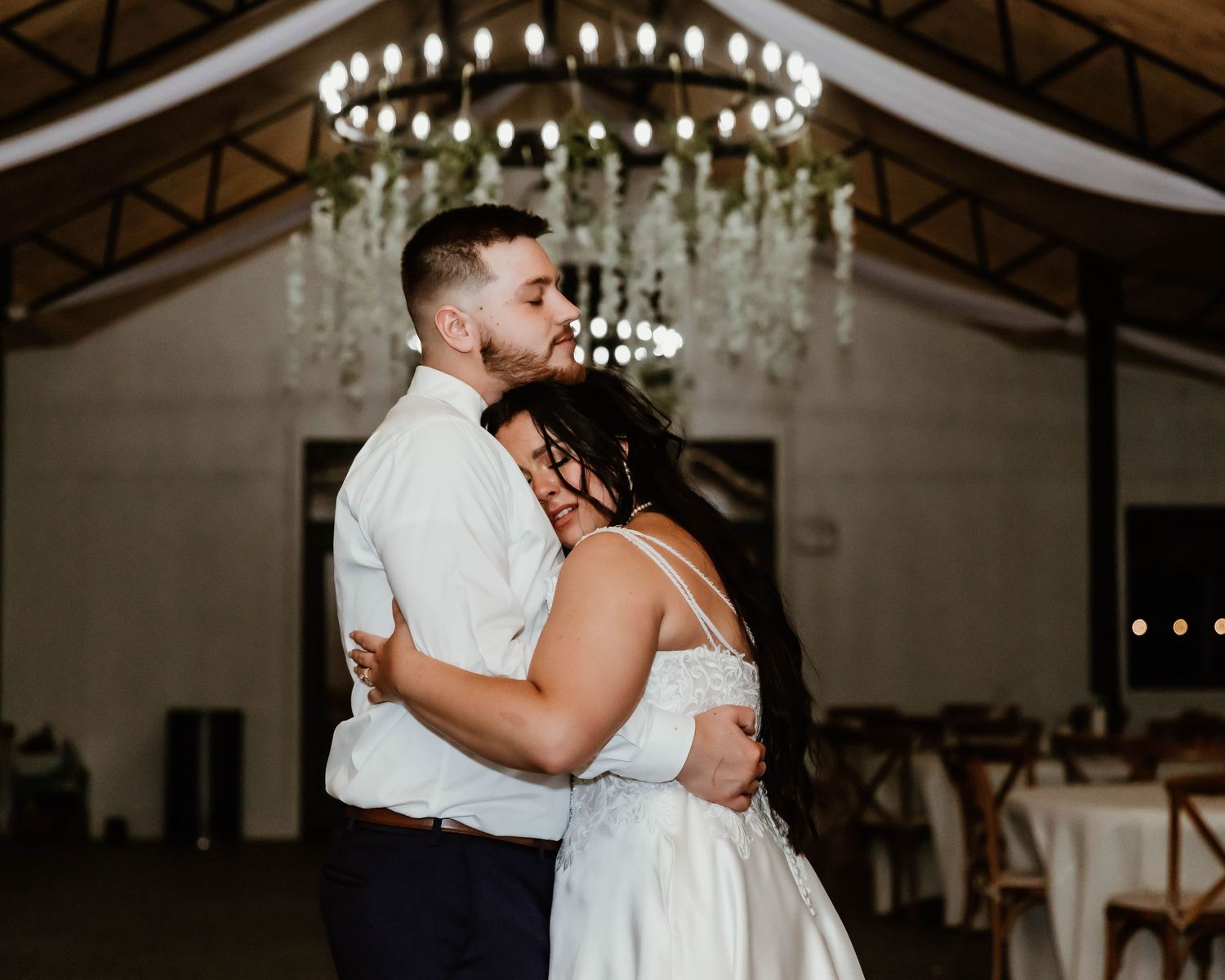Romantic wedding dance under an elegant chandelier in an indoor reception venue.