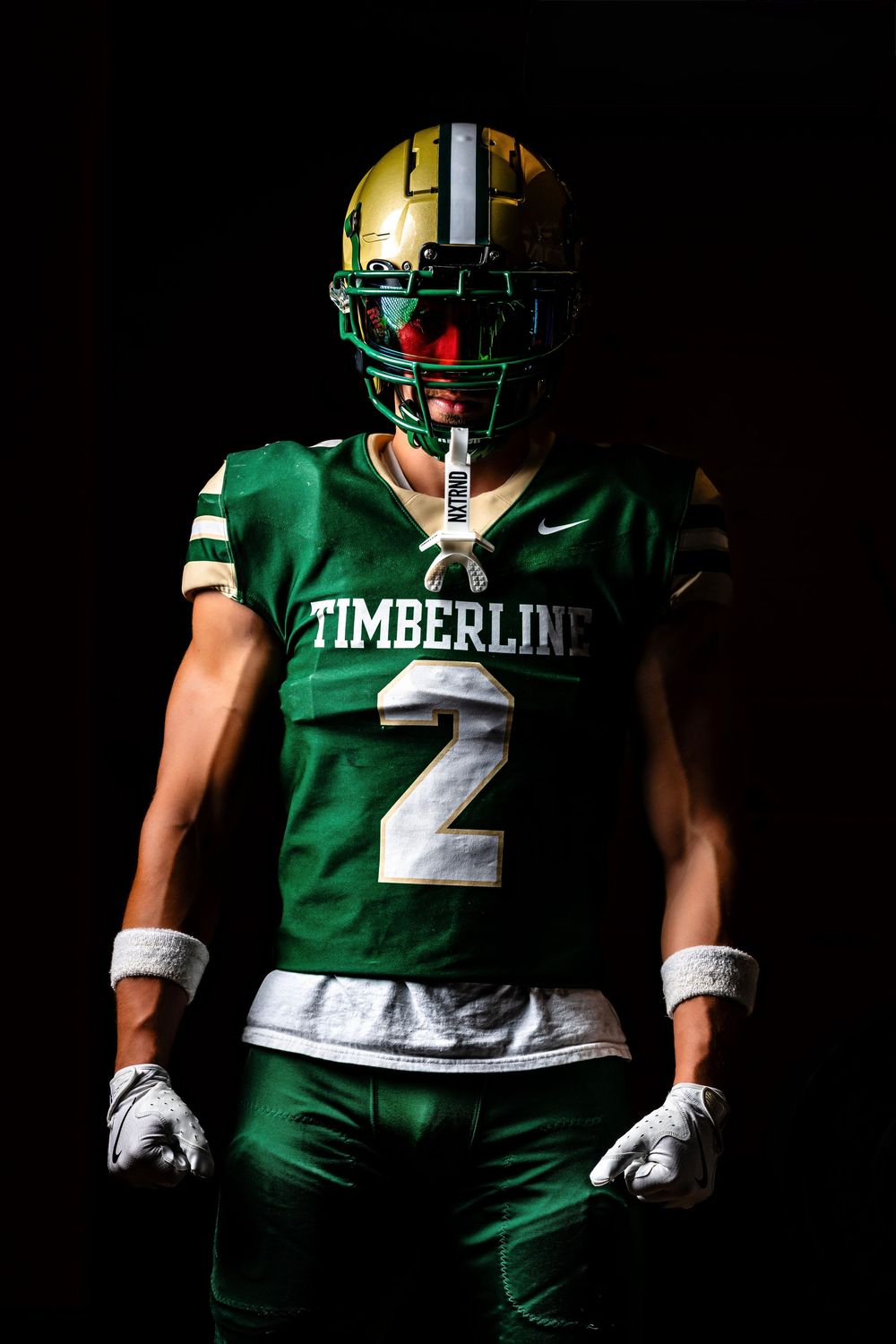 Timberline football player #2 in green jersey and gold helmet poses dramatically against black background.