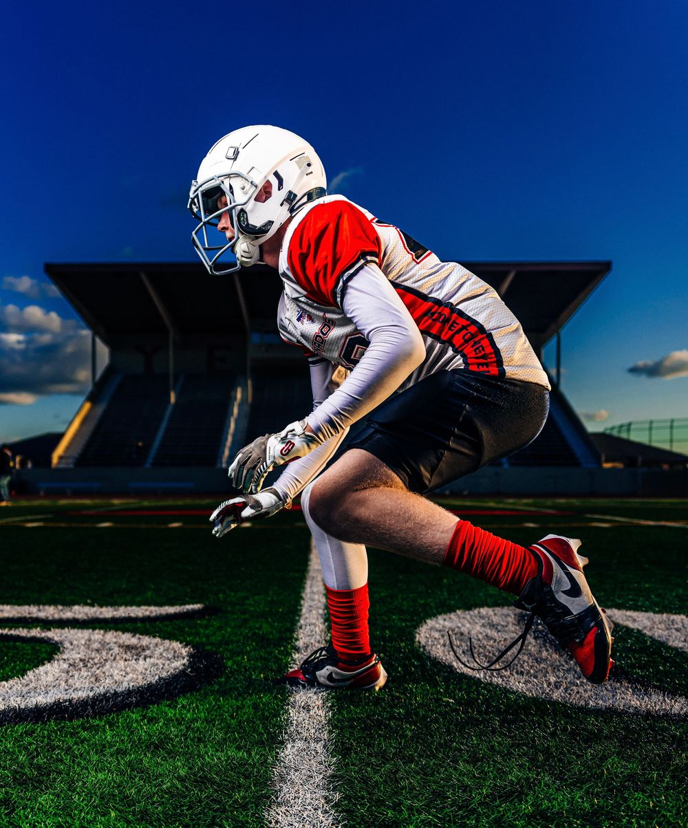 Football player in white and red uniform crouches in ready stance on green turf field.