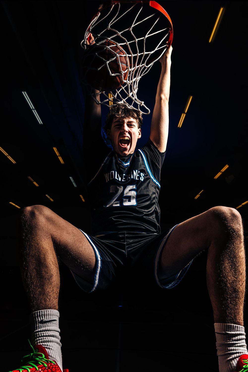 Basketball player #25 dunking and hanging from the net, mouth open in celebration, wearing a dark jersey on black background.