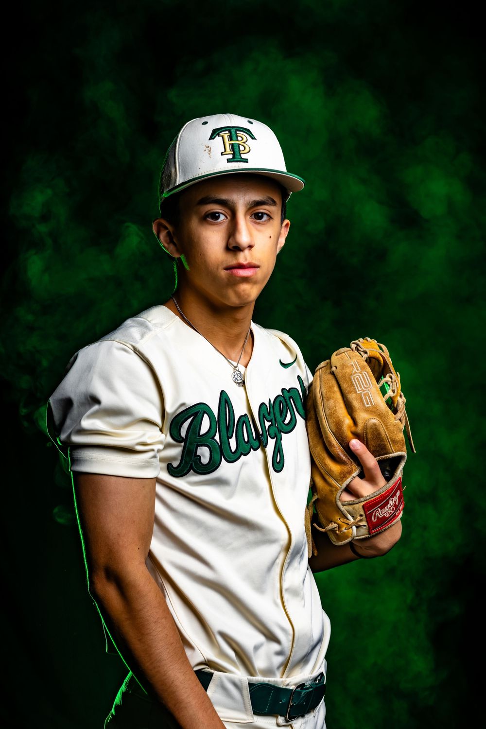 Young baseball player in white Blazers uniform holding a glove, wearing TP cap against green smoke background.