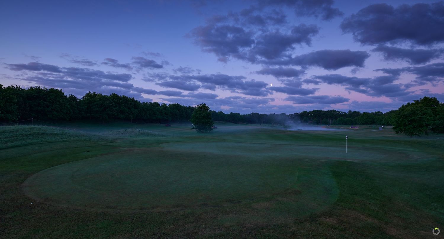 Scenic twilight view of a misty golf course with rolling green fairways under dramatic purple and blue clouds at dusk.