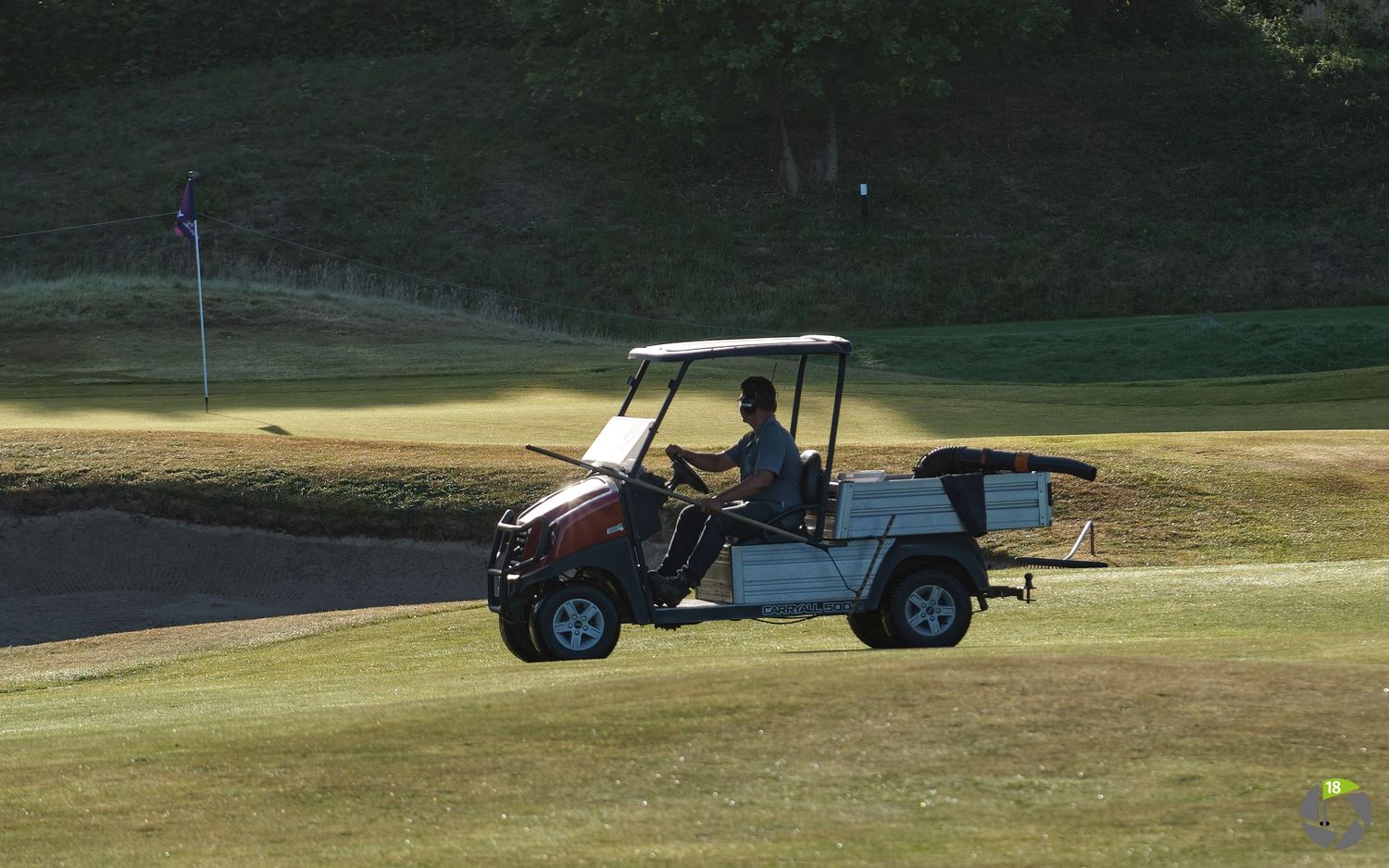 Golf cart driving on a sunny course with late afternoon shadows casting across the green fairway.
