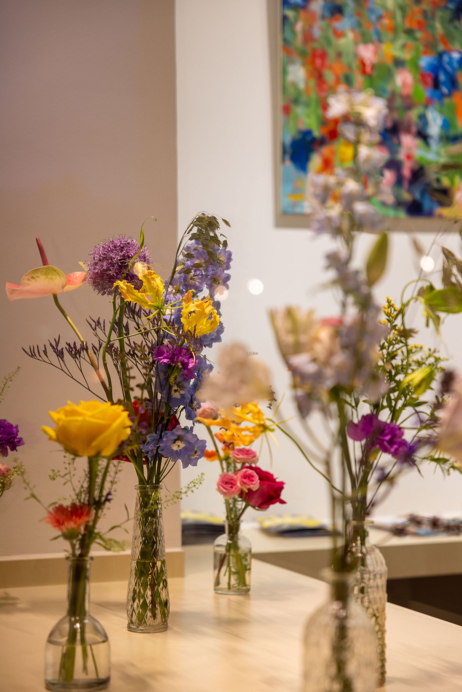 Fresh flower arrangements in glass vases displayed against abstract art gallery backdrop.