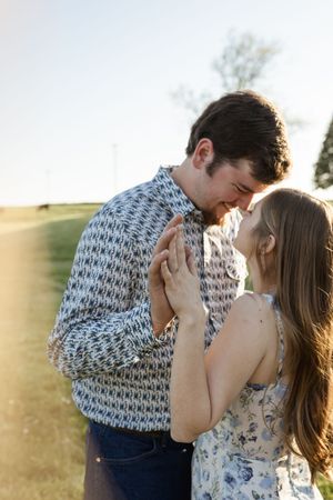 Intimate moment between couple in a floral dress and patterned shirt against golden sunlight.