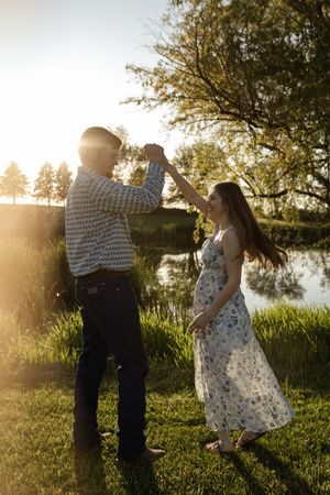 Couple in summer attire sharing romantic moments by a lake at sunset.
