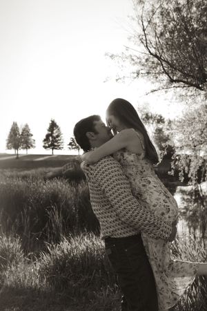 Romantic couple embraces in a sunlit meadow with evergreen trees in the background.