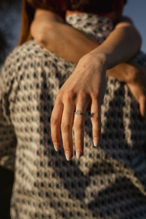 Close-up of hand displaying engagement ring against textured knit sweater.