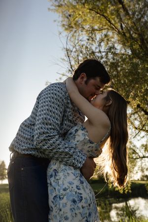 Couple sharing passionate moment in sunlit outdoor setting near water.