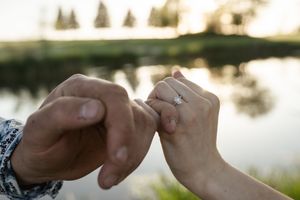 Hands placing an engagement ring during a lakeside proposal.