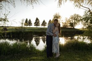 Silhouetted couple against sunset sky with lake and trees in view.