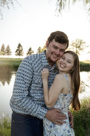 Happy couple embracing outdoors with a lake and trees in the background.