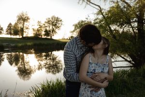 A romantic sunset engagement photo session by a serene lake with trees silhouetted against the golden sky.