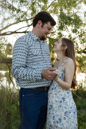 A couple shares intimate moments in a floral dress and patterned shirt against a natural outdoor backdrop.