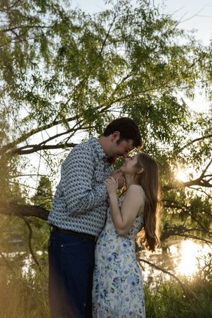Romantic sunset engagement photos with a couple embracing under tree branches.