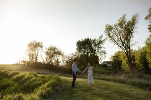 Wide landscape shot of a couple's silhouette against a sunset in an open field.